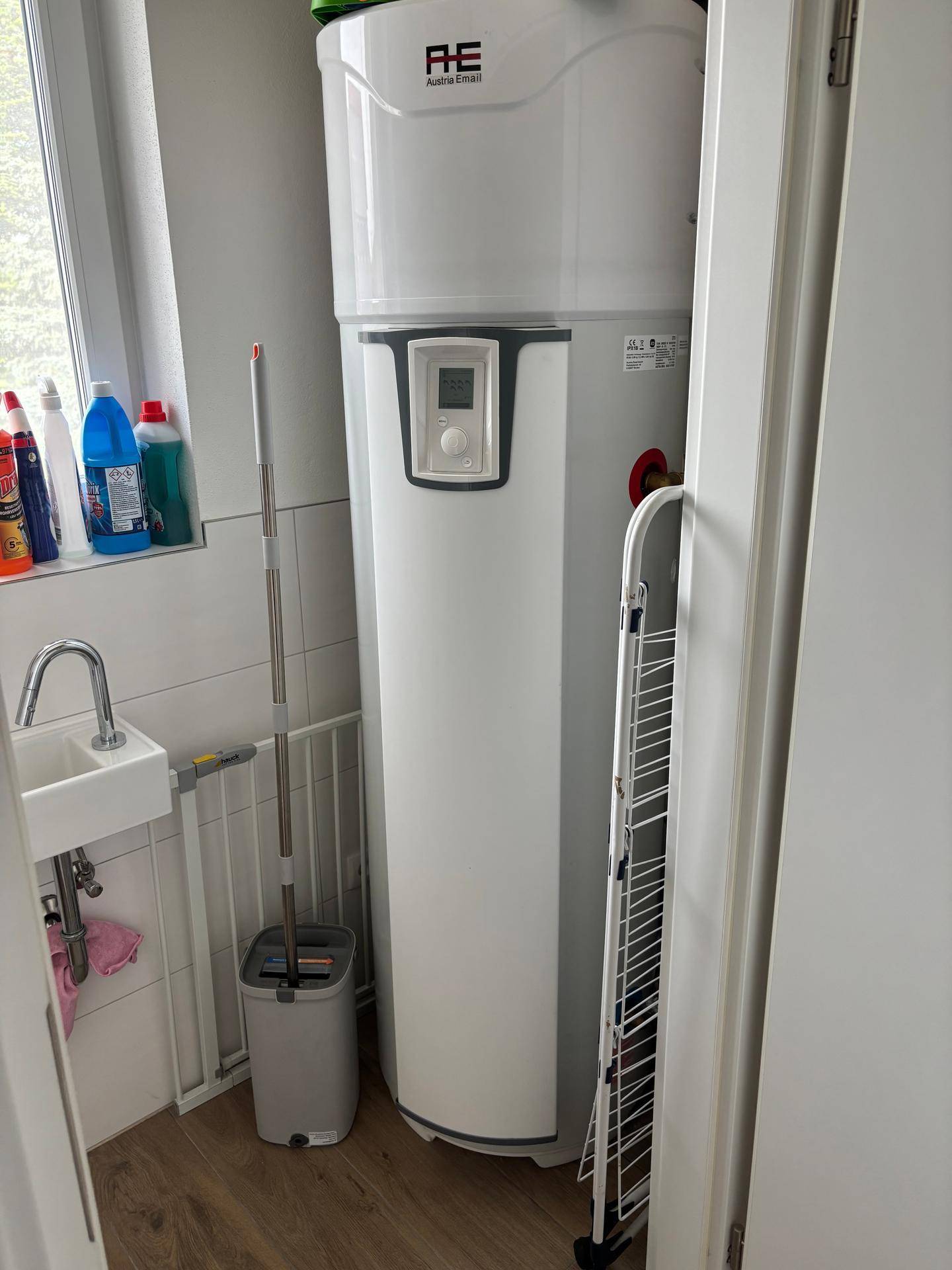 Hauswirtschaftsraum mit großem Warmwasserspeicher, kleinem Waschbecken und Fenster.