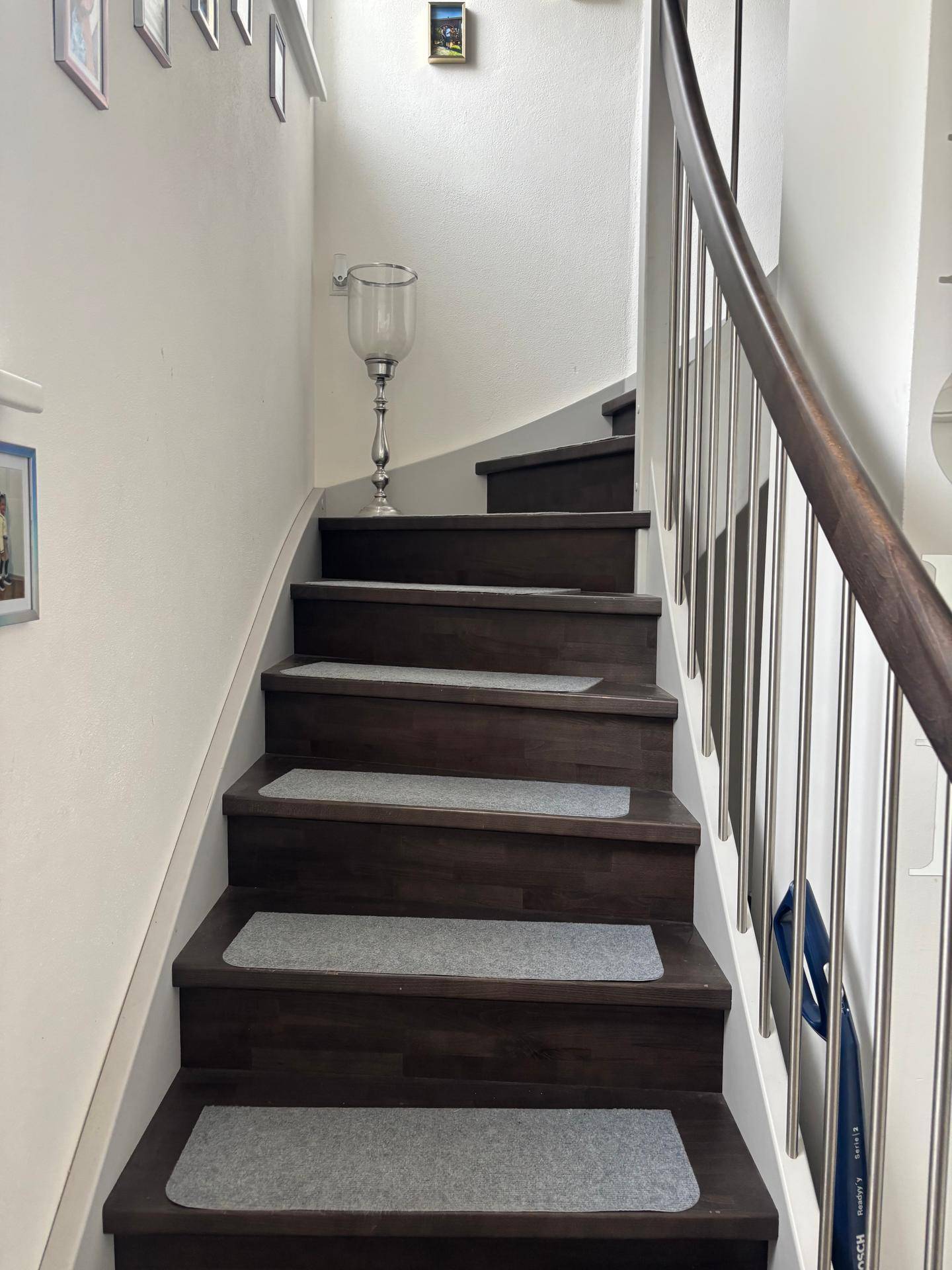 Moderne Holztreppe mit Metallgeländer und hellen Stufenmatten in einem Flur.