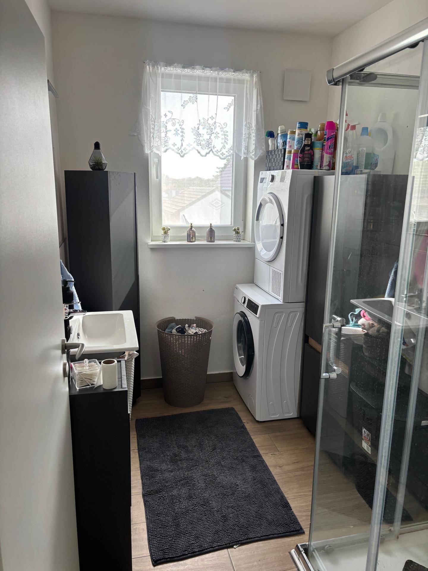 Funktionaler Hauswirtschaftsraum mit Waschmaschine, Trockner, Duschkabine und Fenster.