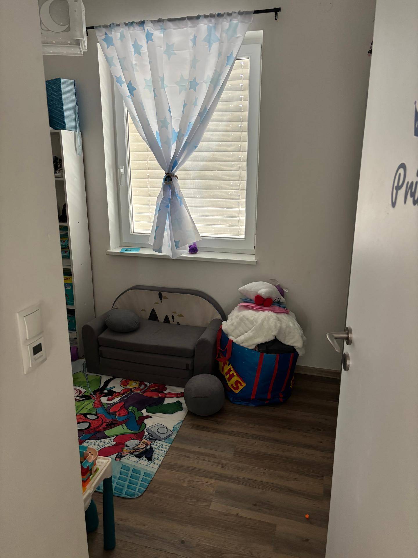 Kinderzimmer mit kleinem Sofa, Spielteppich und einem Fenster mit Sternenvorhängen.