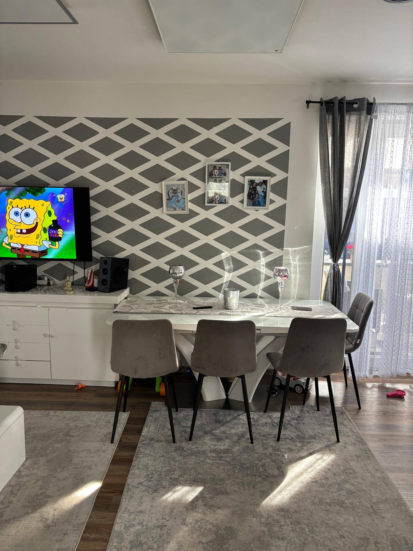 Heller Wohn-Essbereich mit modernem Esstisch, Teppich und einem Fernseher an der Wand.