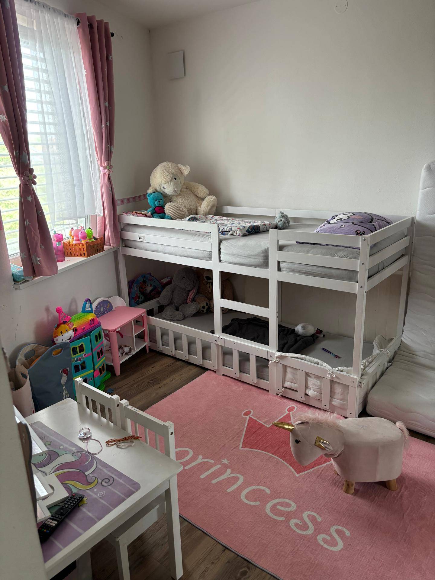 Helles Kinderzimmer mit Etagenbett, rosa Teppich und Spielzeug.