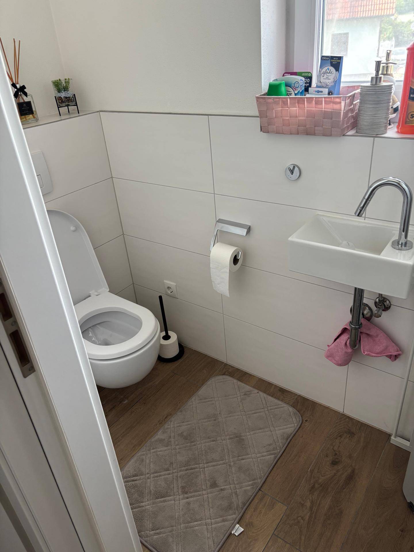 Helles Gäste-WC mit wandhängender Toilette, kleinem Waschbecken und Fenster.