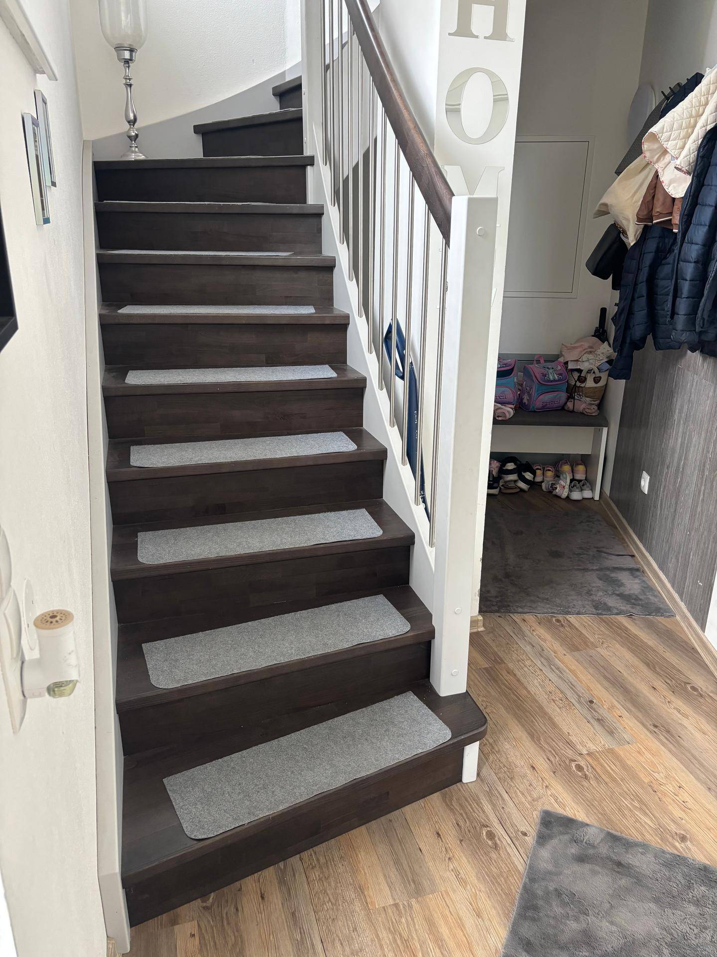 Dunkle Holztreppe mit hellen Stufenmatten und weißem Geländer in einem modernen Flur.
