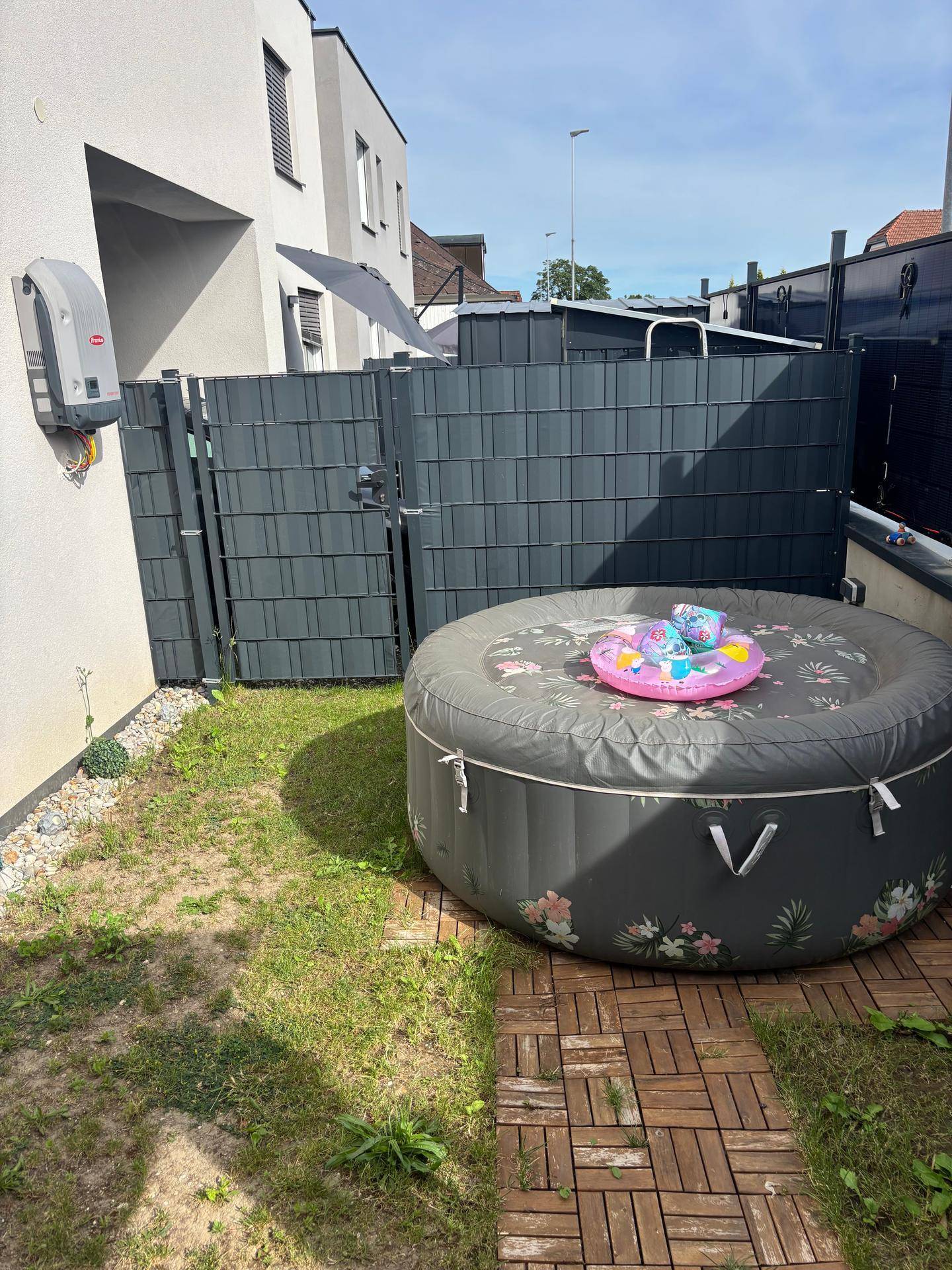 Gartenbereich mit aufblasbarem Whirlpool, Holzdielen und einem Zaun.
