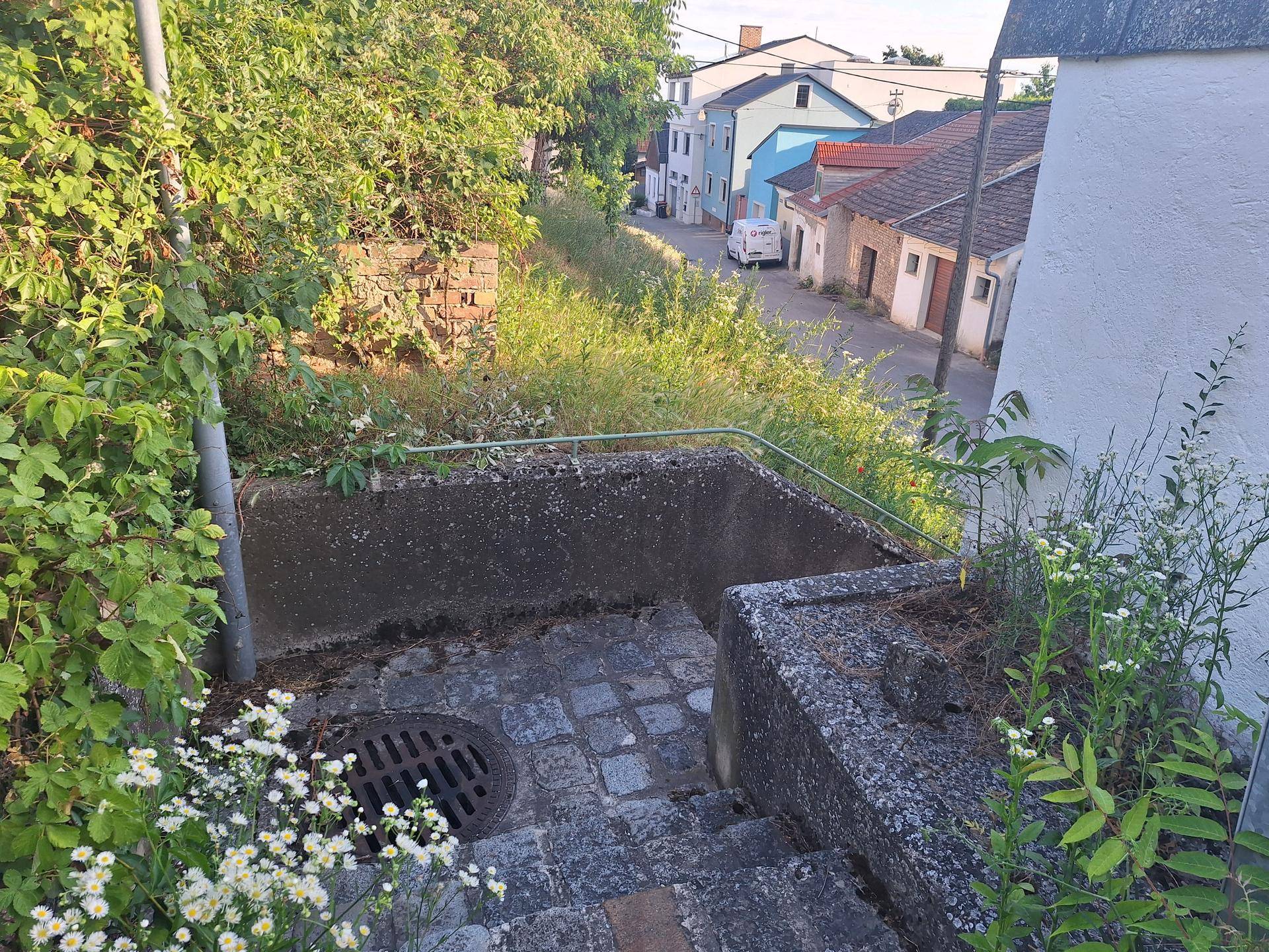Steintreppe mit Metallgeländer führt hinunter zu einer Straße mit Häusern im Hintergrund.