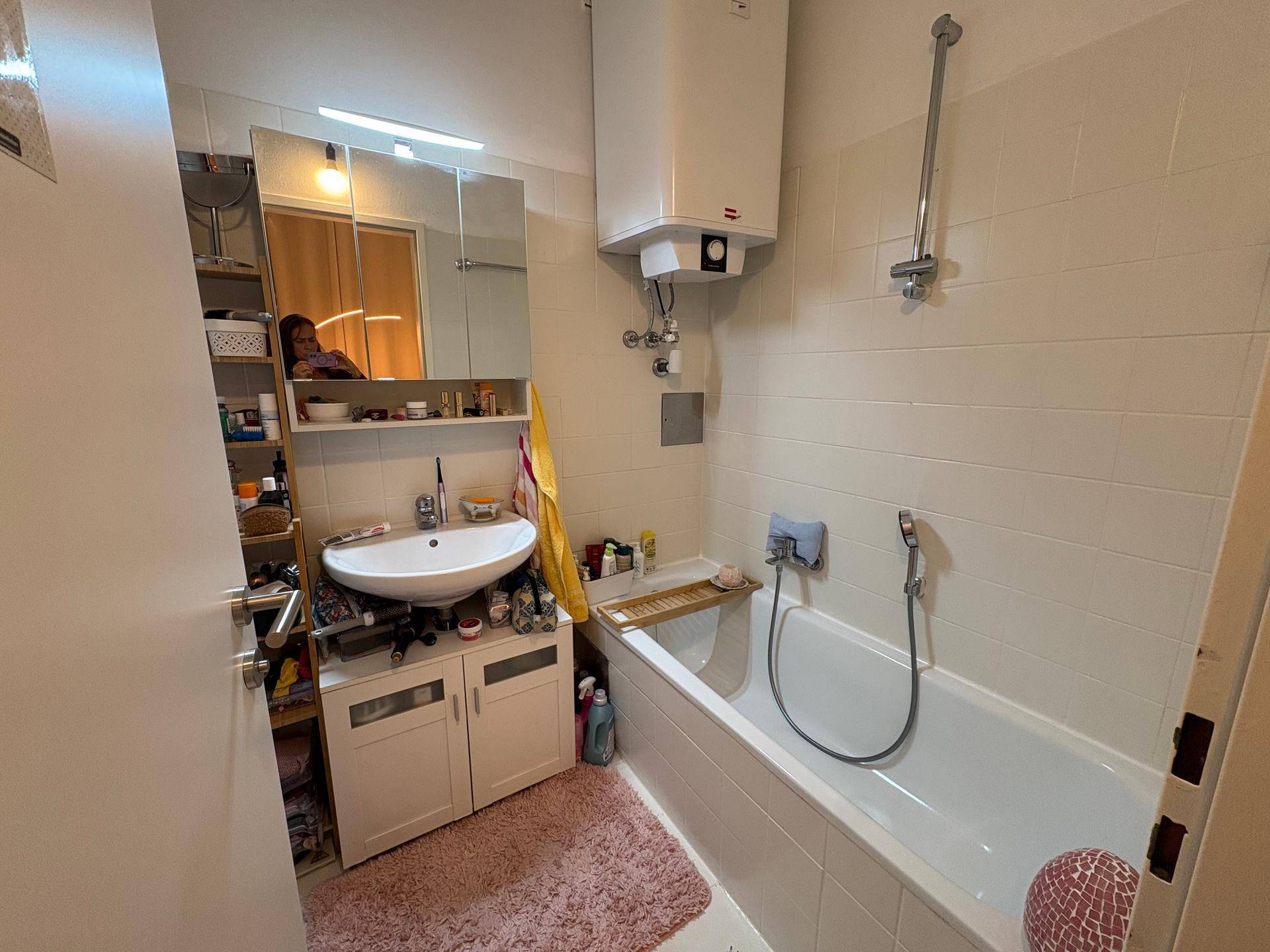 Funktionales Badezimmer mit Badewanne, Waschbecken und Spiegelschrank, hell gefliest.