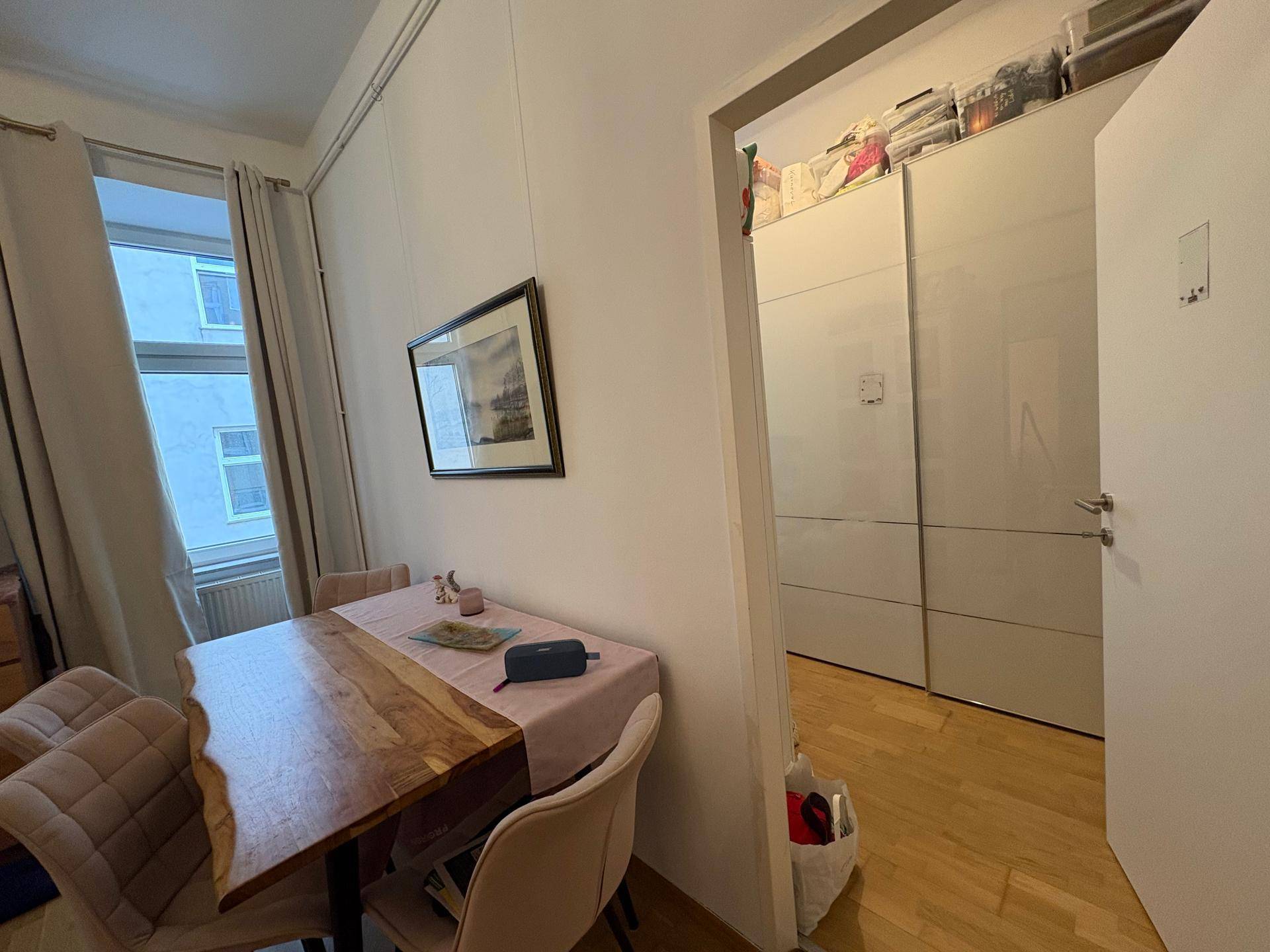 Essbereich mit Holztisch und Stühlen, angrenzend an einen Raum mit praktischen Einbauschränken.