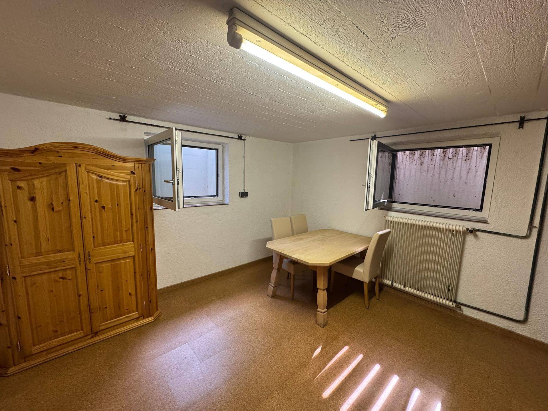 Kellerraum mit Holzkleiderschrank, Esstisch und kleinen Fenstern, ideal als Hobbyraum.