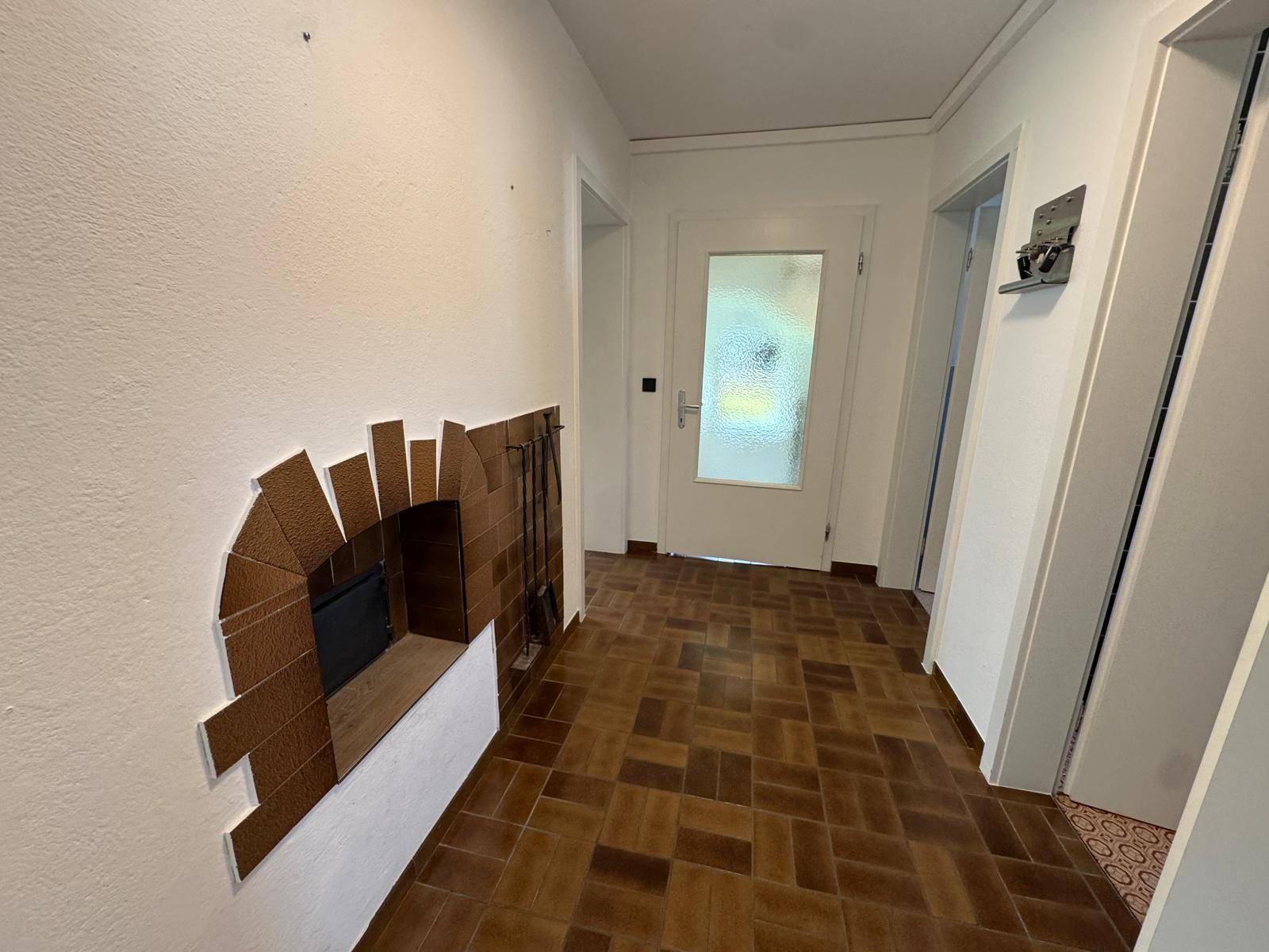 Flur mit braunem Fliesenboden und einer dekorativen Kaminöffnung, die zum Eingang führt.