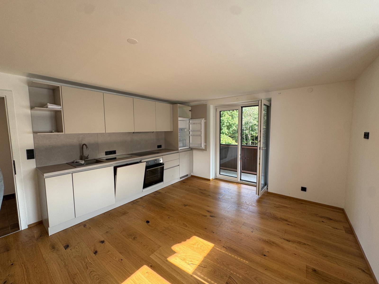 Offene Küche mit Holzboden und Zugang zu einem Balkon, umgeben von grüner Natur.