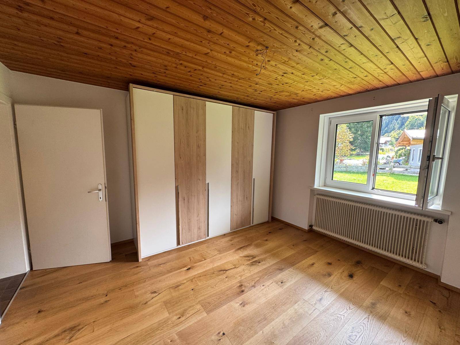 Schlafzimmer mit Holzboden, Holzdecke und großem Einbauschrank, bietet Blick ins Grüne.