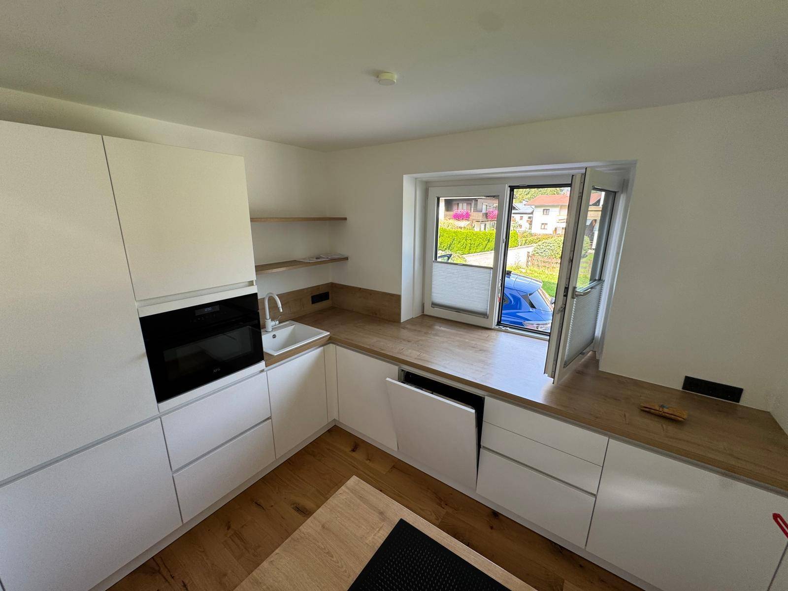 Helle Einbauküche mit weißen Fronten, Holzdetails und Fenster mit Blick auf die Umgebung.