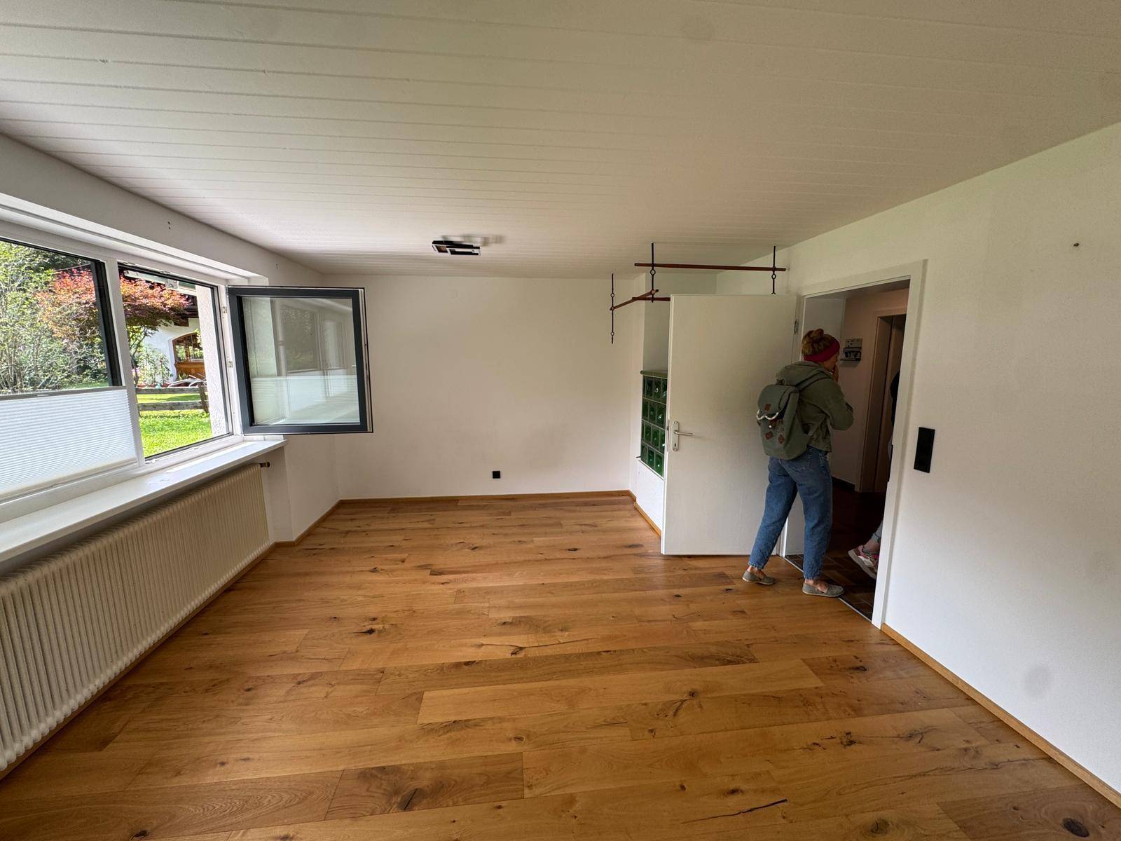 Geräumiges Wohnzimmer mit Holzboden, großem Fenster und Blick ins Grüne.