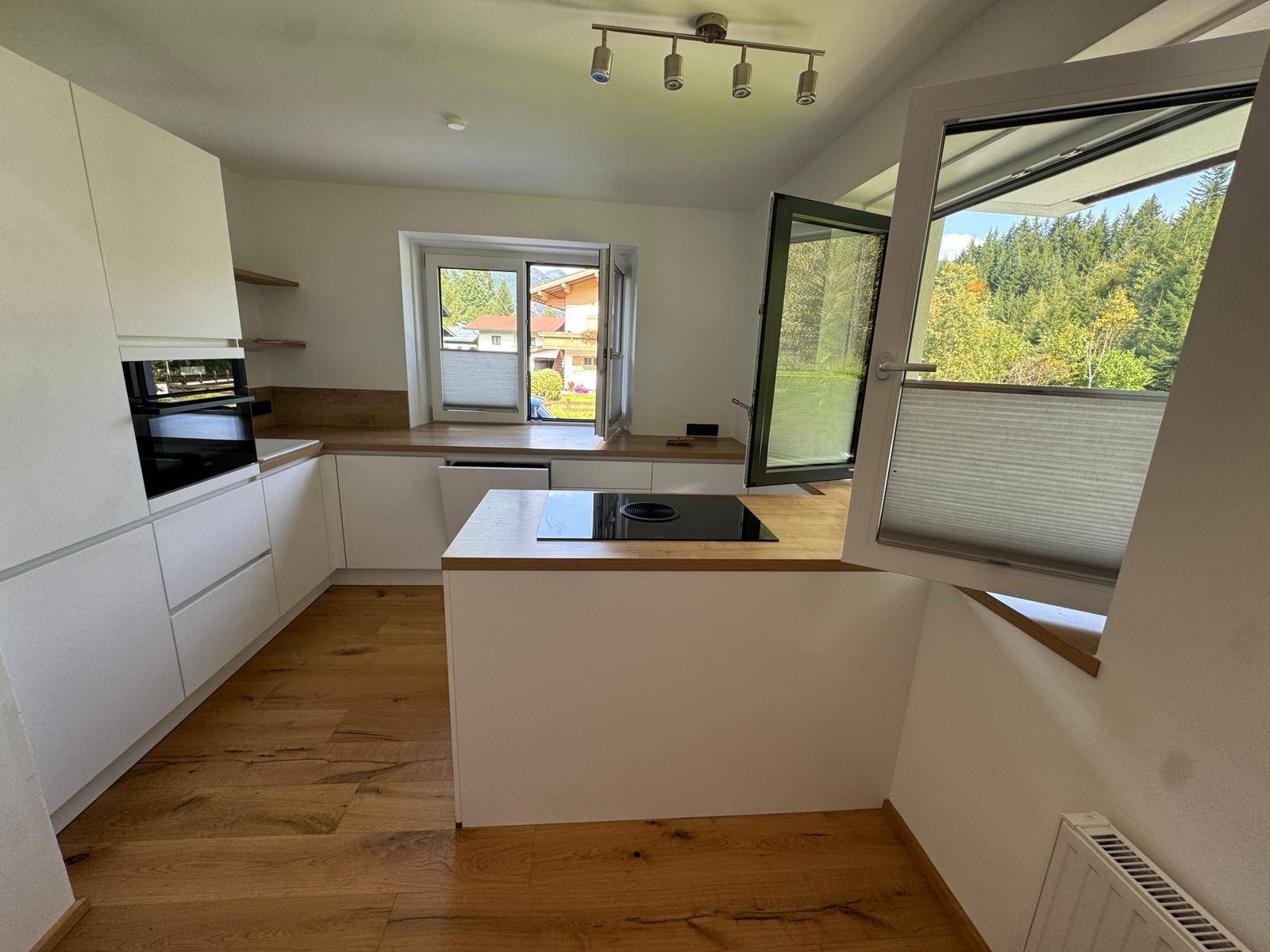Moderne Küche mit weißen Schränken, Holzarbeitsplatten und Induktionskochfeld mit Bergblick.