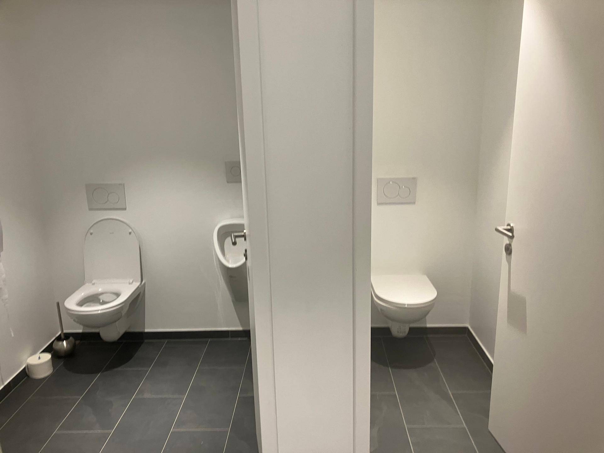 Zwei separate Toilettenkabinen mit Wand-WCs und dunklen Bodenfliesen in einem modernen Waschraum.