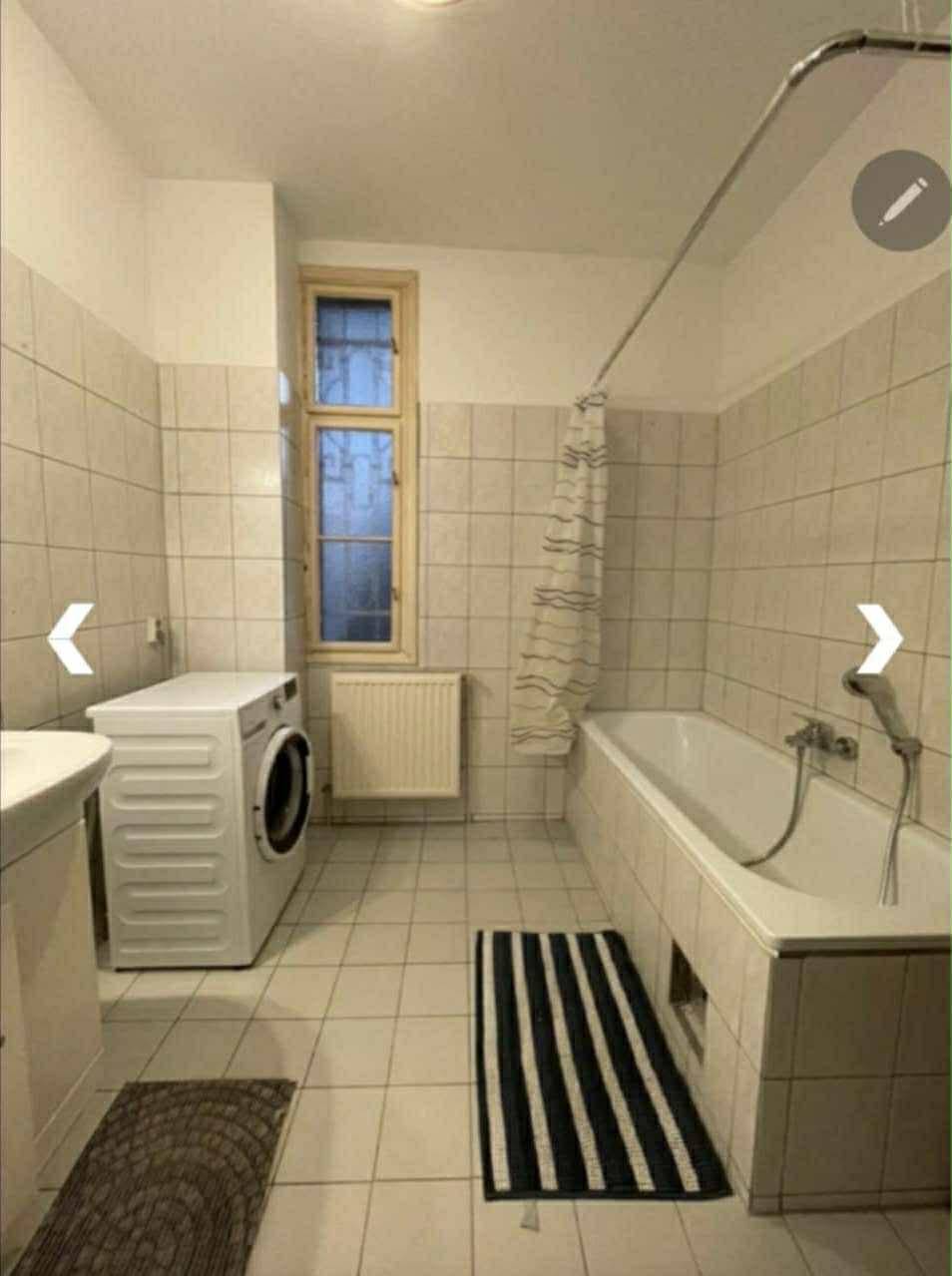 Badezimmer mit Badewanne, Waschbecken, Waschmaschine und Fenster für Tageslicht.
