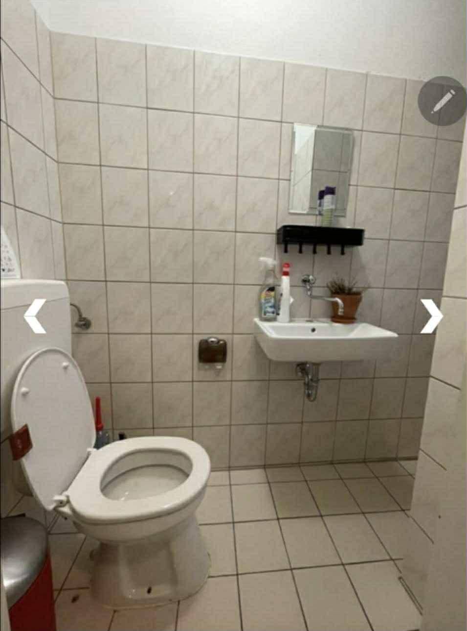 Kleines WC mit hellen Fliesen, Toilette und einem einfachen Waschbecken.