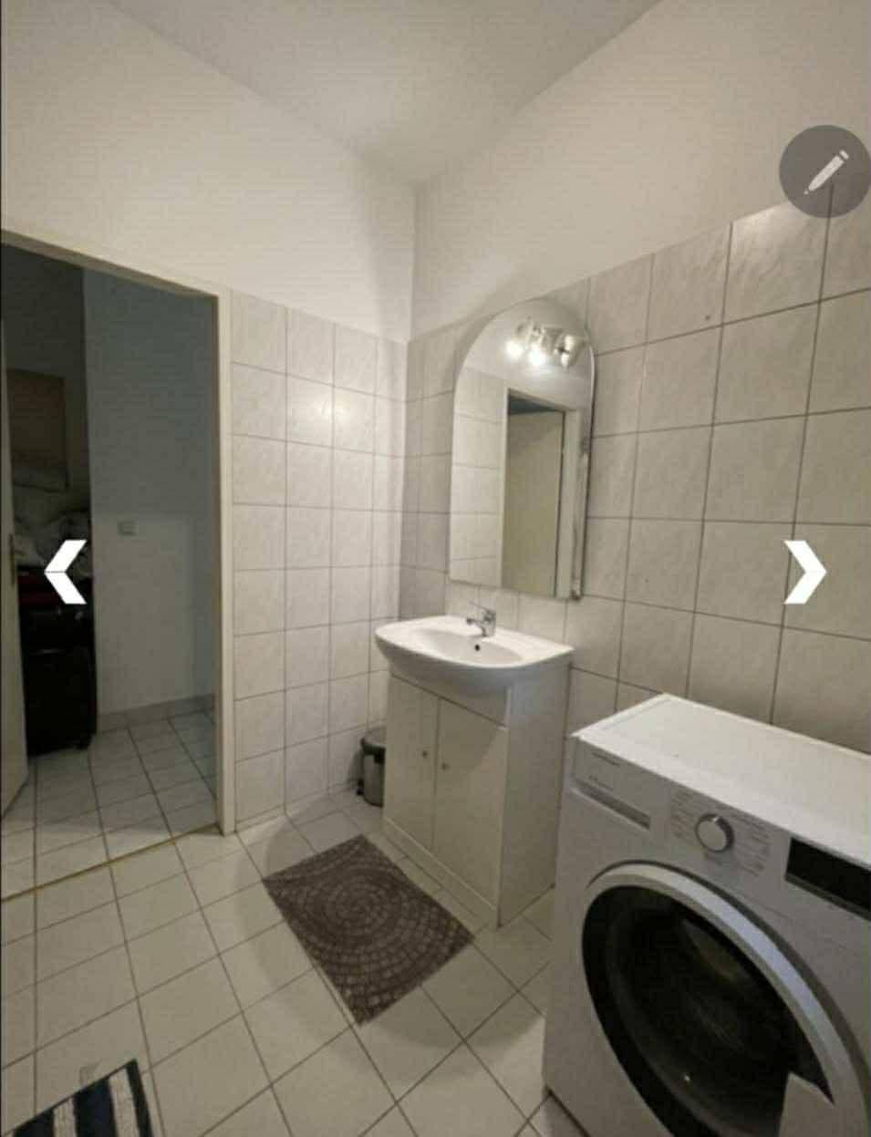 Badezimmer mit Waschbecken, Spiegel und Waschmaschine, hell gefliest.