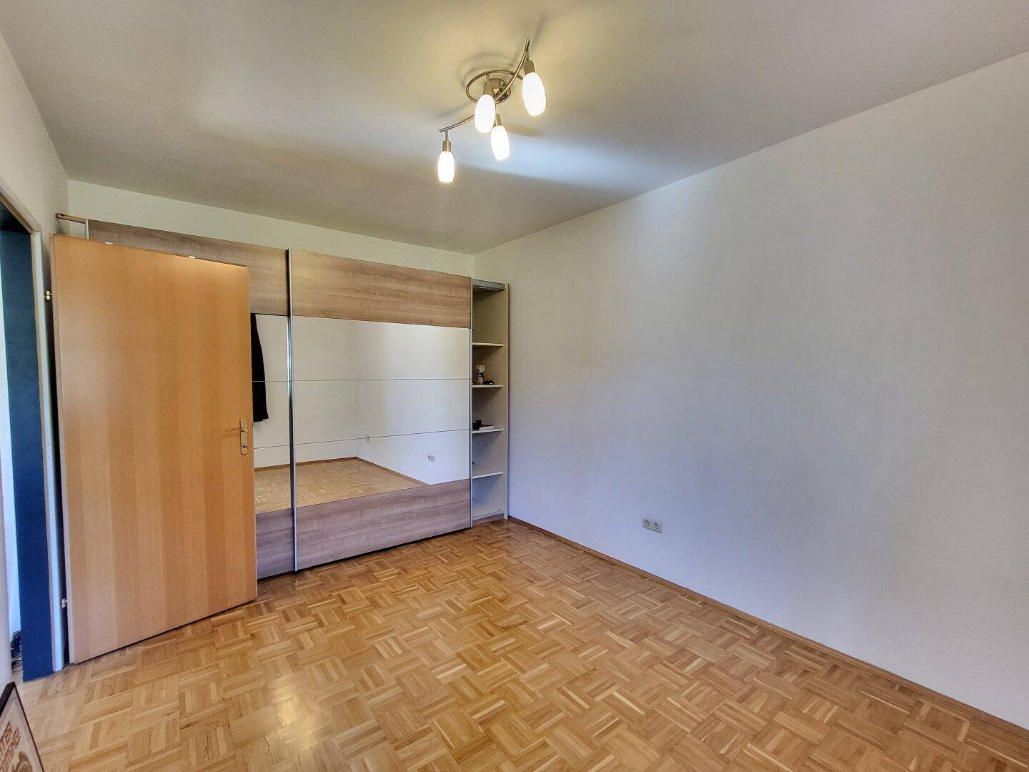 Geräumiges Schlafzimmer mit Parkettboden und großem Spiegelschrank.