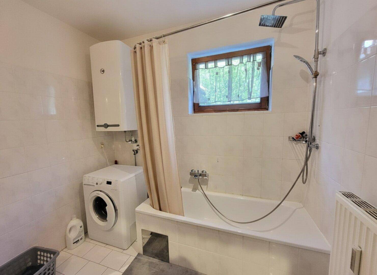 Badezimmer mit Badewanne, Dusche, Waschmaschine und Fenster.