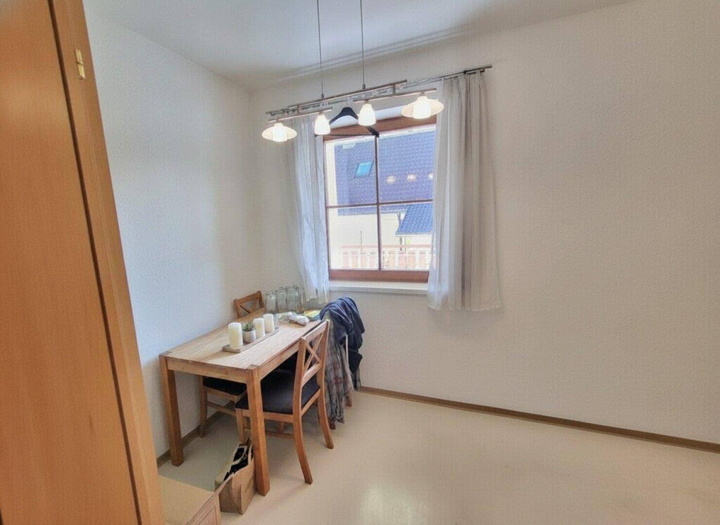 Kleiner Essbereich mit Holztisch und Stühlen, beleuchtet durch ein Fenster.