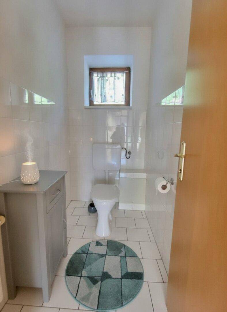 Kleines Gäste-WC mit weißen Fliesen, Fenster und einem modernen Waschtischunterschrank.