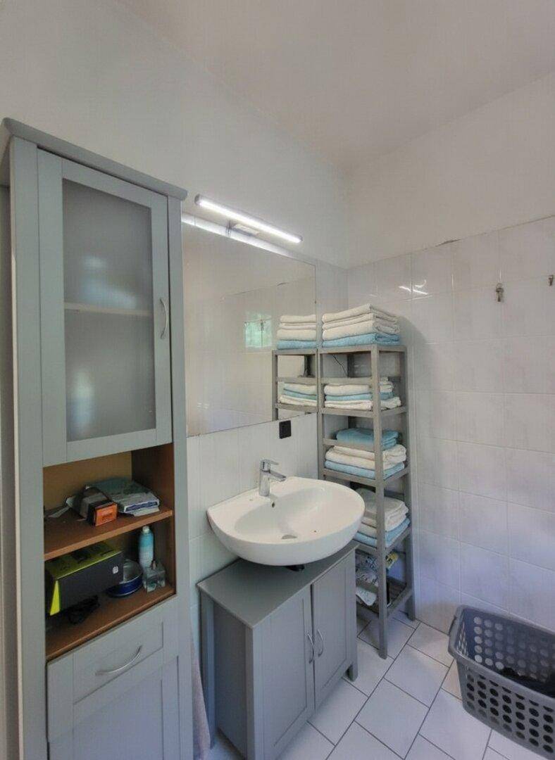 Badezimmer mit Waschtisch, großem Spiegel und praktischen Regalen für Handtücher.