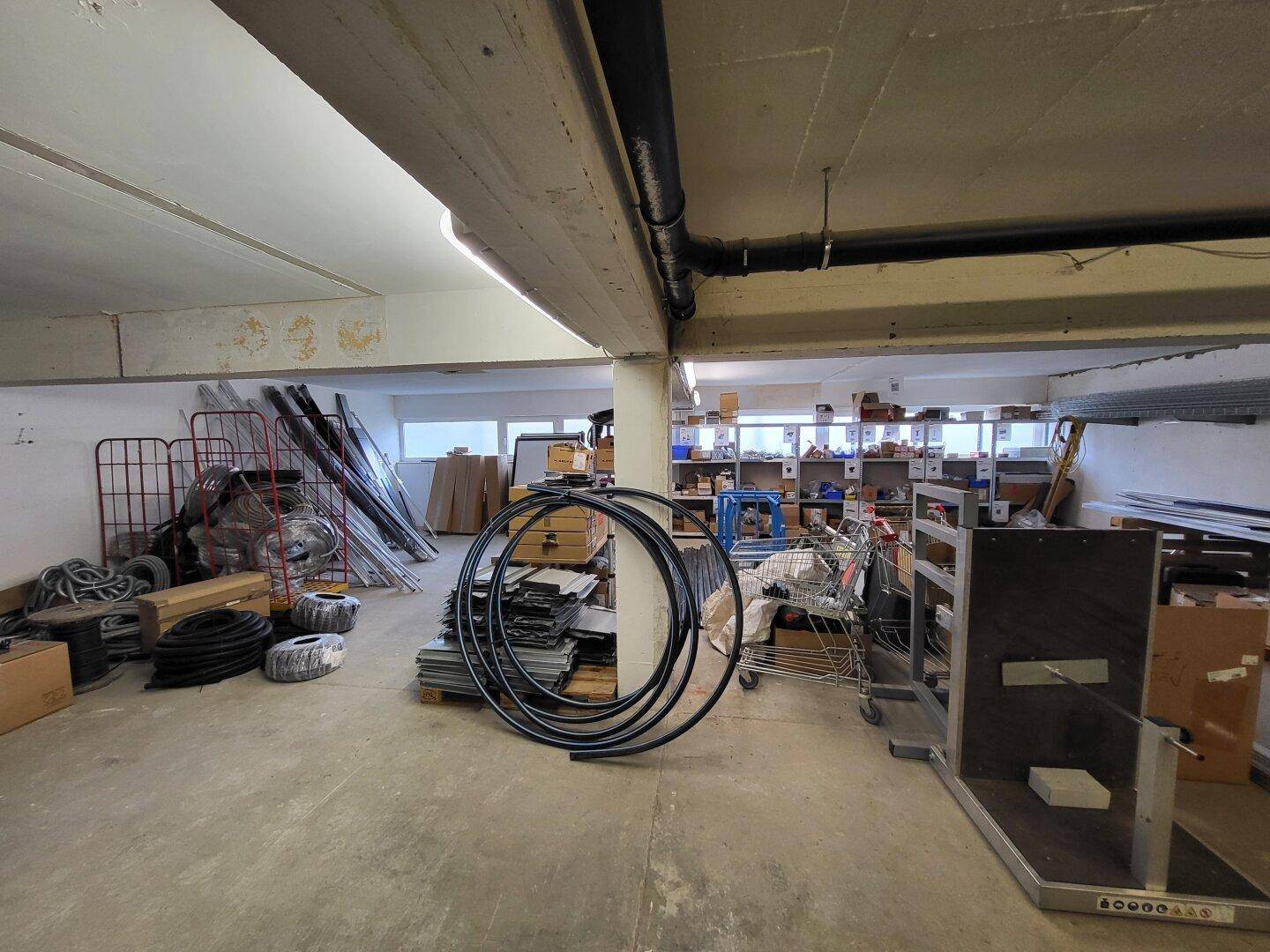 Geräumiger Lagerbereich mit Betonboden, Regalen im Hintergrund und sichtbaren Rohren an der Decke.