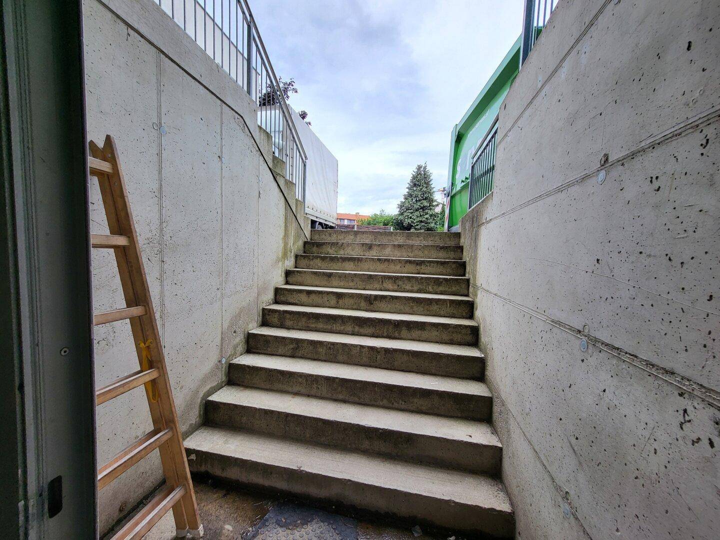 Außentreppe aus Beton, die von einem unteren Bereich nach oben führt, umgeben von Betonwänden.