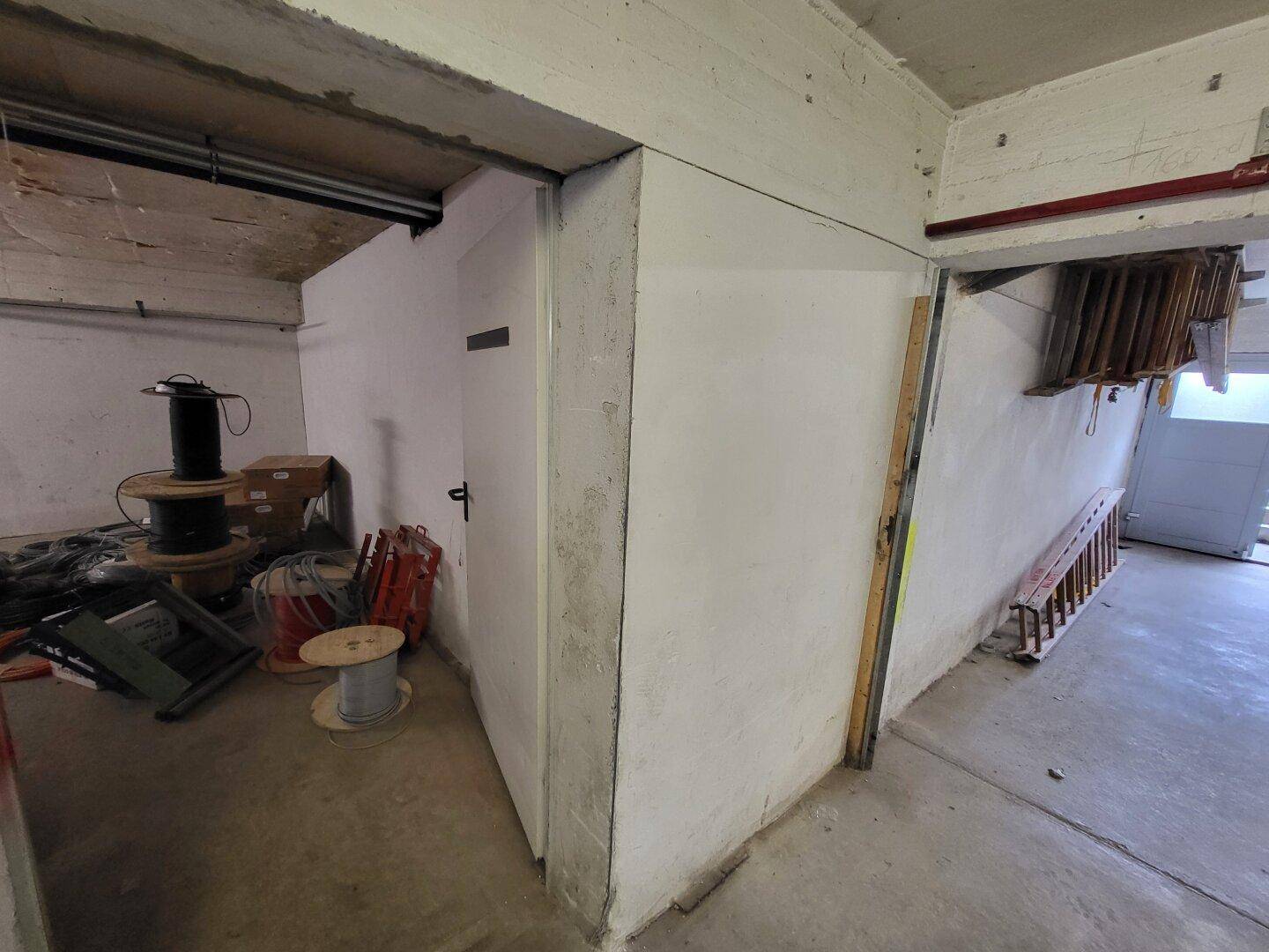 Ecke eines Lagerraums mit einer geschlossenen Tür, Betonwänden und Decke sowie gelagerten Materialien.