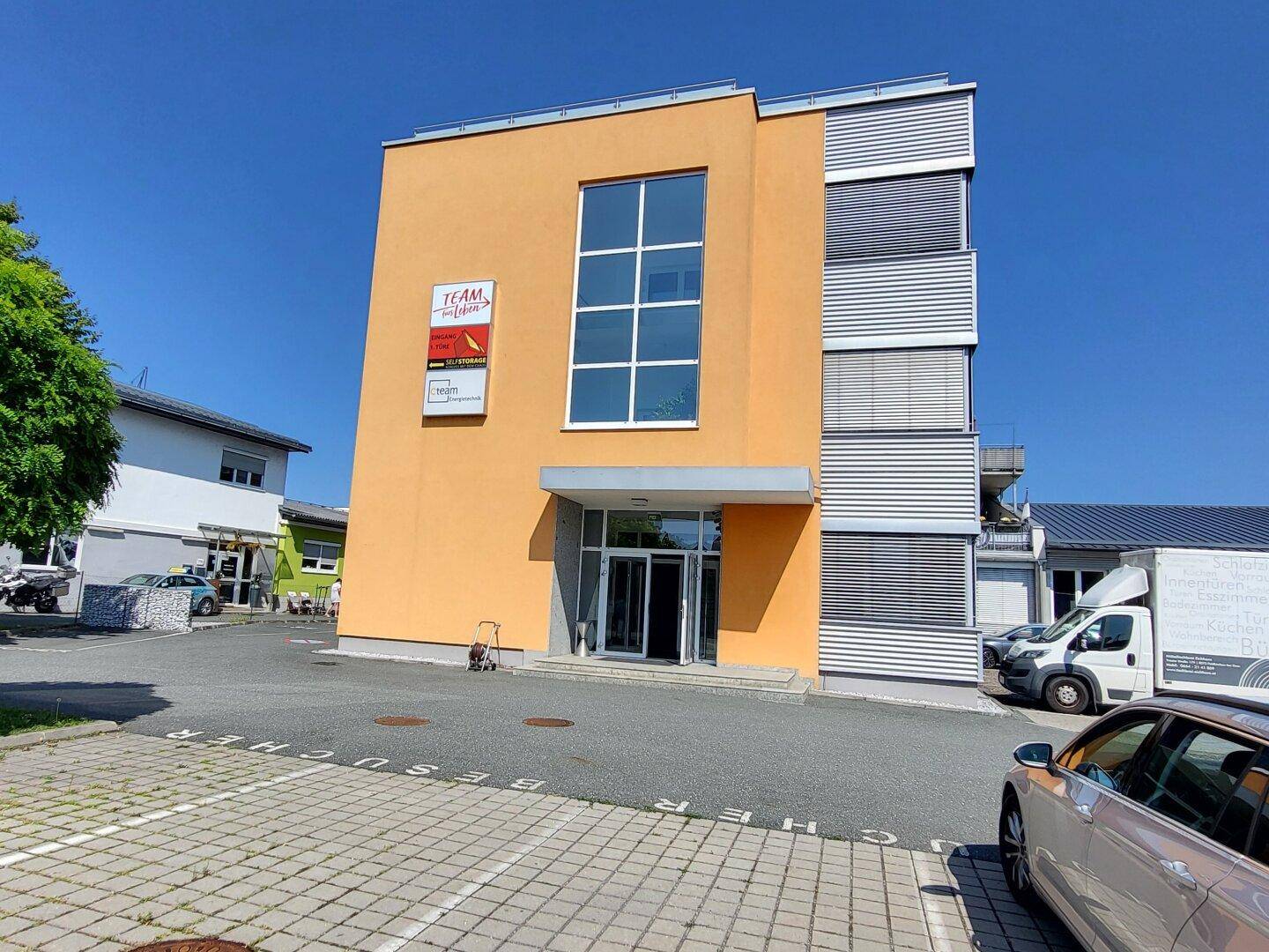 Modernes Geschäftsgebäude mit auffälliger orangefarbener Fassade, großen Fenstern und Parkplätzen.