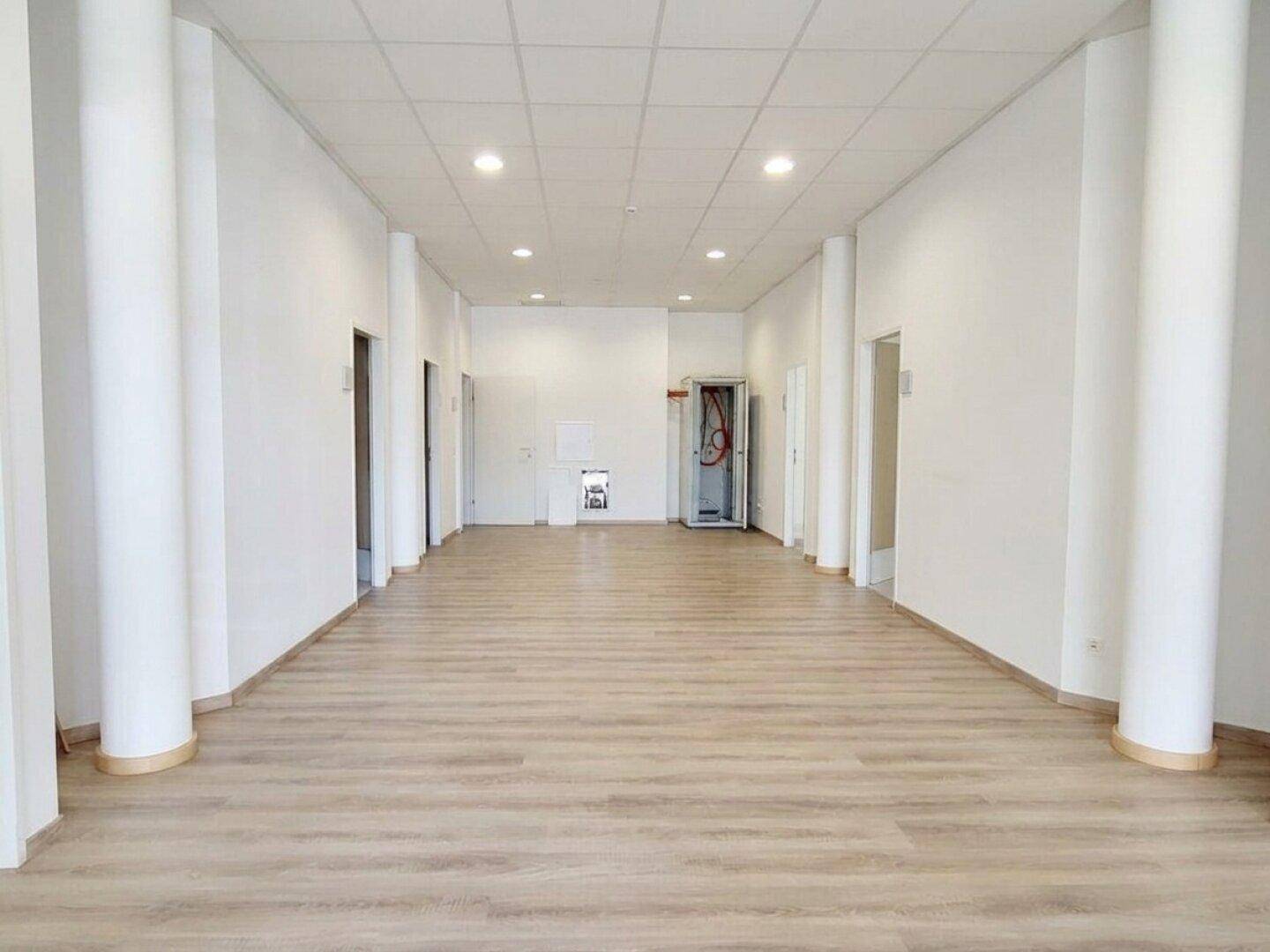 Langer, heller Flur oder Großraumbüro mit Säulen und modernem Laminatboden in einem Neubau.