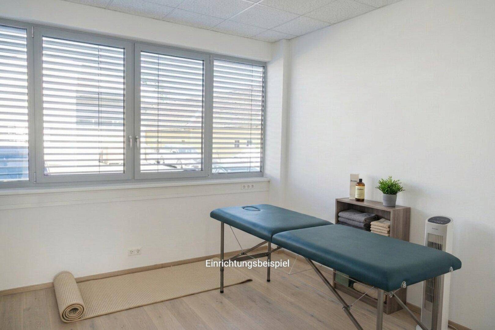 Behandlungsraum mit Massageliege, Yogamatte und großen Fenstern, ideal für Wellness oder Therapie.
