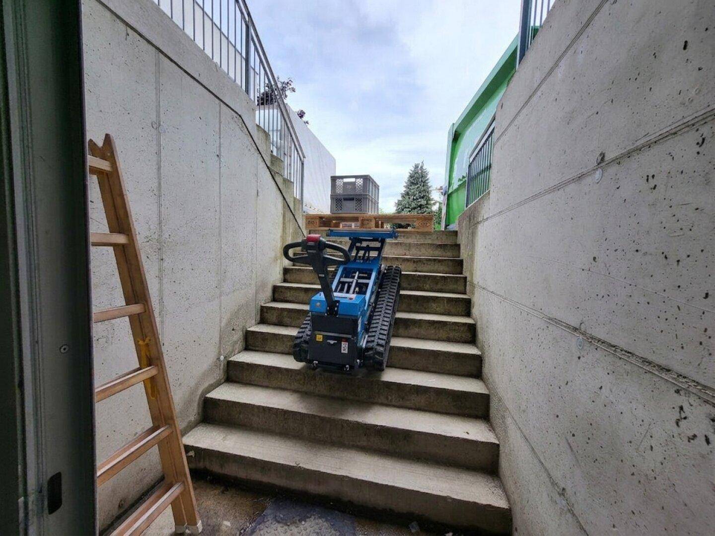 Betontreppe als Zugangsbereich mit einem kleinen Raupenfahrzeug und einer Holzleiter.
