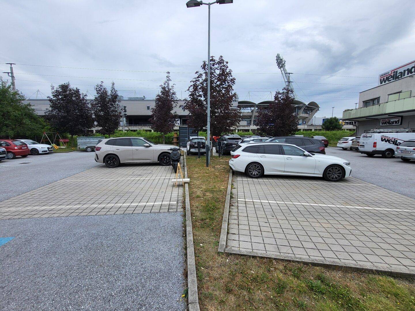 Großer Parkplatz mit mehreren Autos und einer Ladestation für Elektrofahrzeuge.