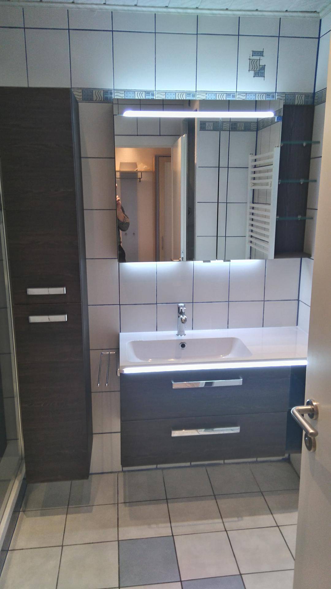 Modernes Badezimmer mit Waschtischunterschrank, Spiegel, hellen Fliesen und praktischem Stauraum.