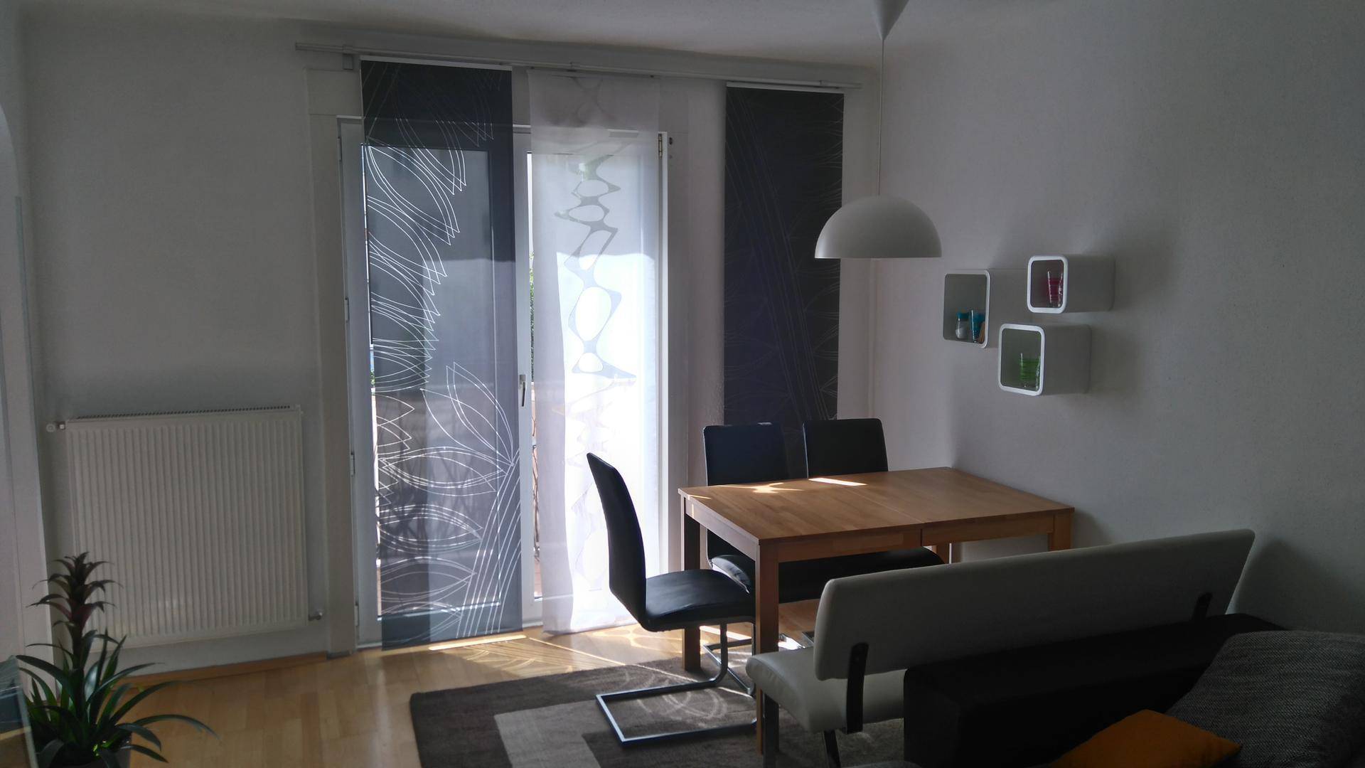 Heller Wohn- und Essbereich mit Holztisch, bequemer Sitzbank und Zugang zum Balkon.