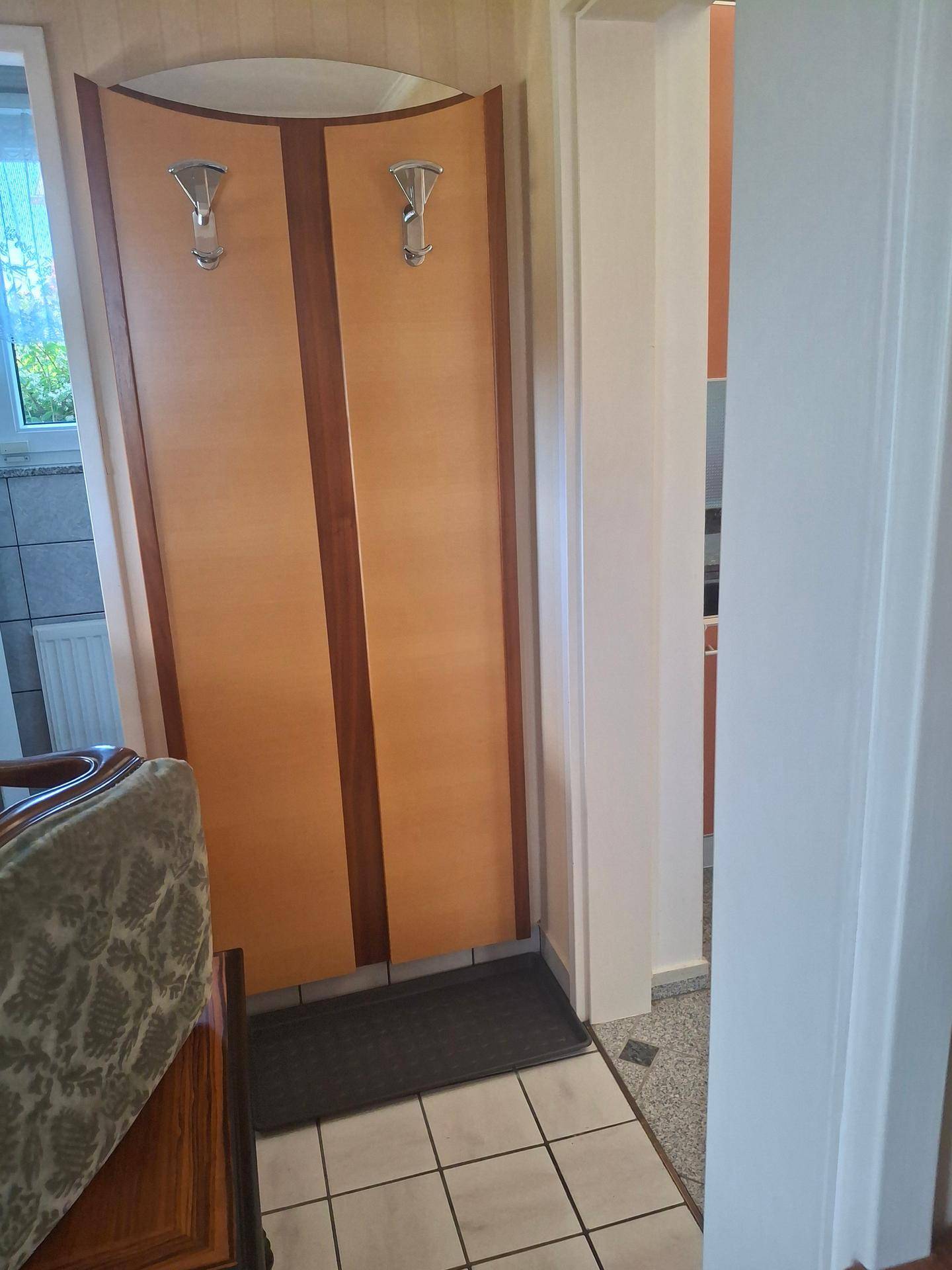 Flur mit hellem Fliesenboden und einer Garderobe aus Holz.