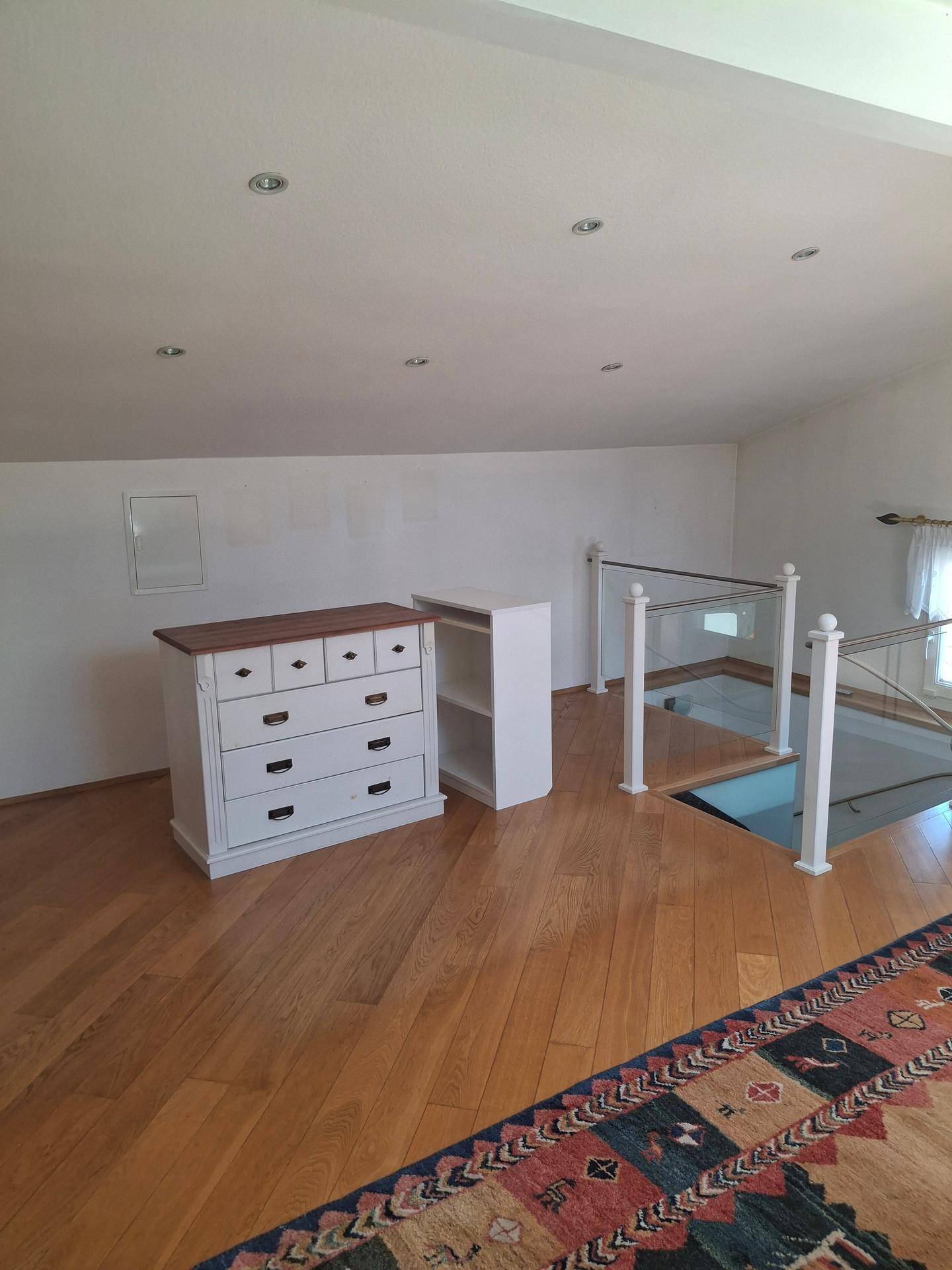 Offener Dachgeschossbereich mit Holzboden, weißer Kommode und Blick auf das Treppenhaus.