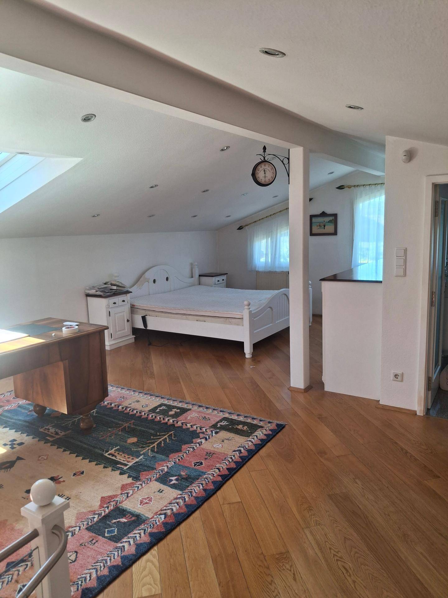 Helles Schlafzimmer im Dachgeschoss mit Holzboden, Schreibtisch und Dachfenstern.