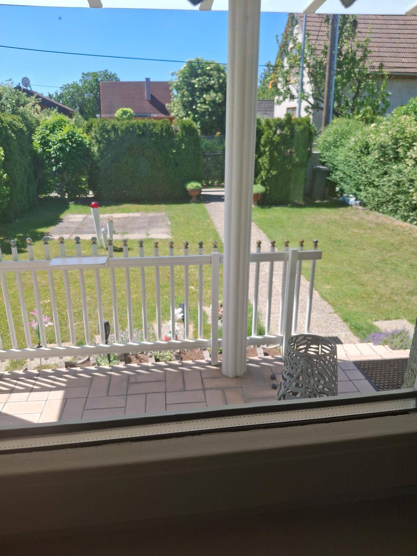 Blick von der Terrasse in den Garten mit gepflastertem Bereich und weißem Zaun.
