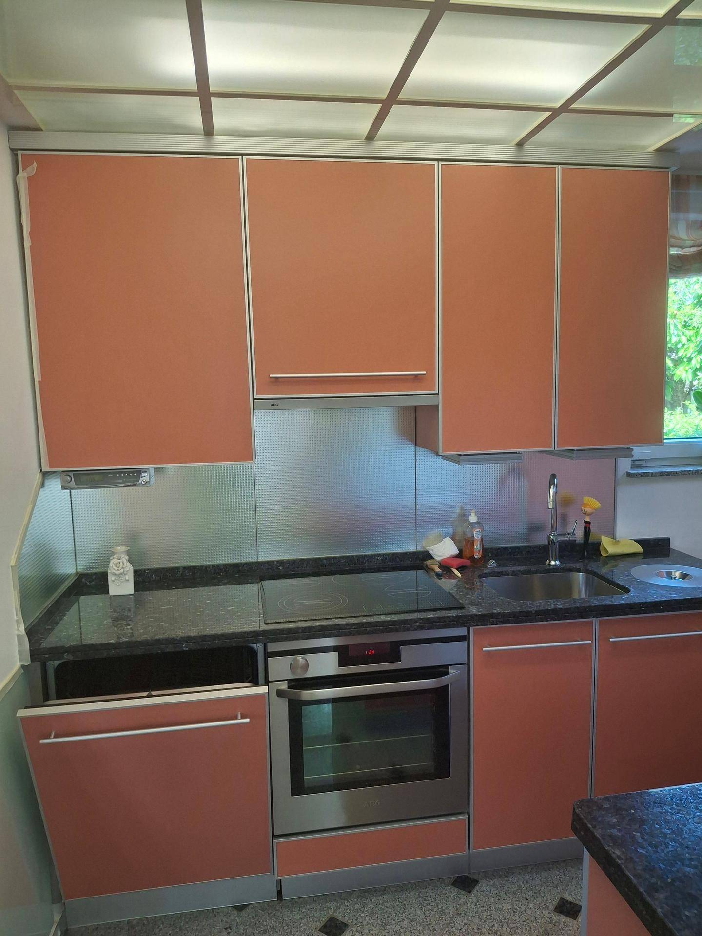 Küche mit orangefarbenen Schränken, dunkler Arbeitsplatte, integriertem Backofen und Spüle.