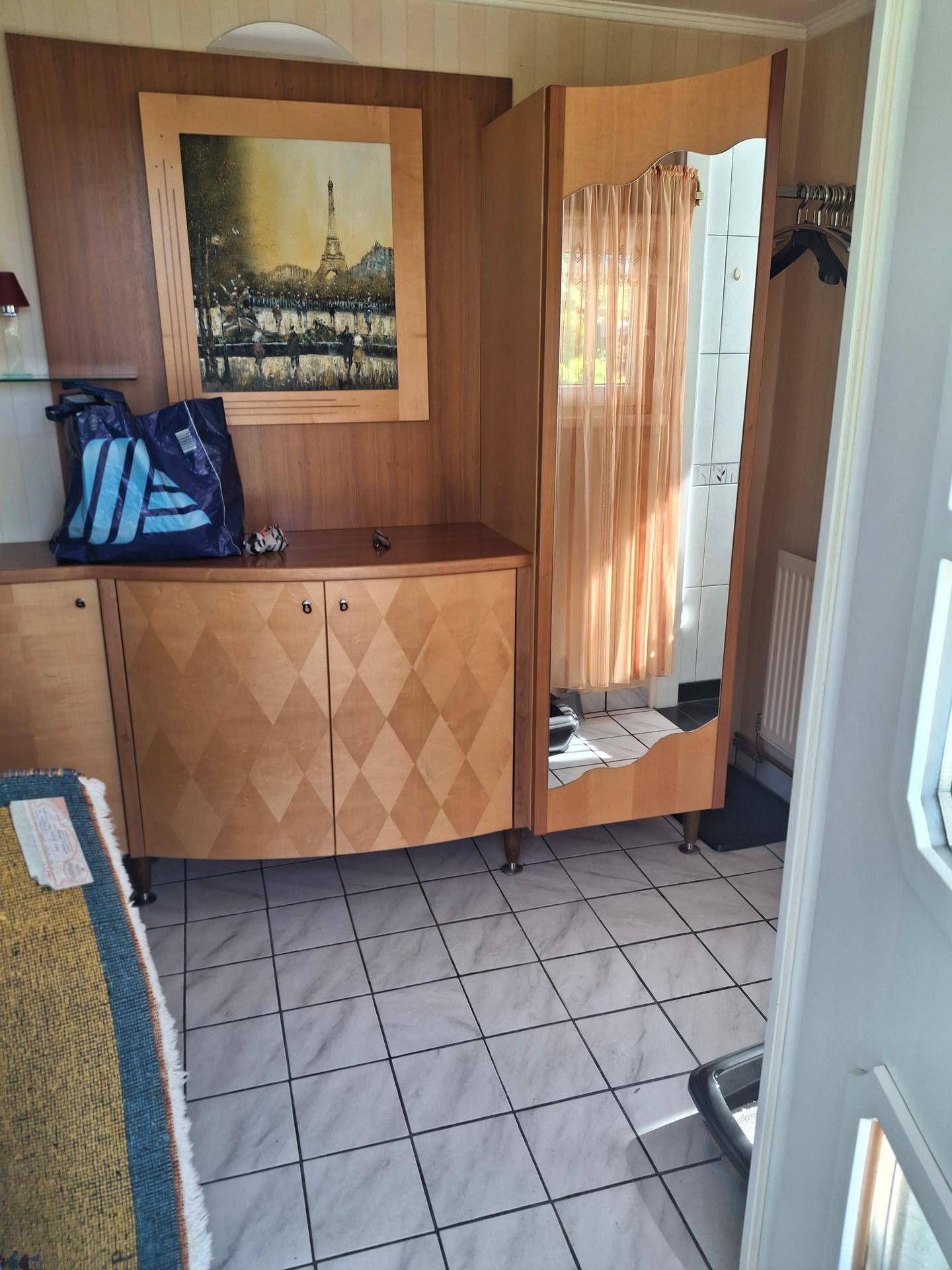 Eingangsbereich mit Holzschrank, Spiegel und hellem Fliesenboden.