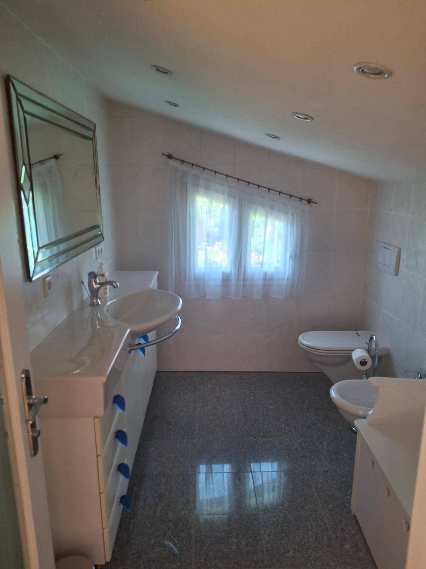 Modernes Badezimmer mit weißen Fliesen, langem Waschtisch, Toilette, Bidet und Dachschräge.