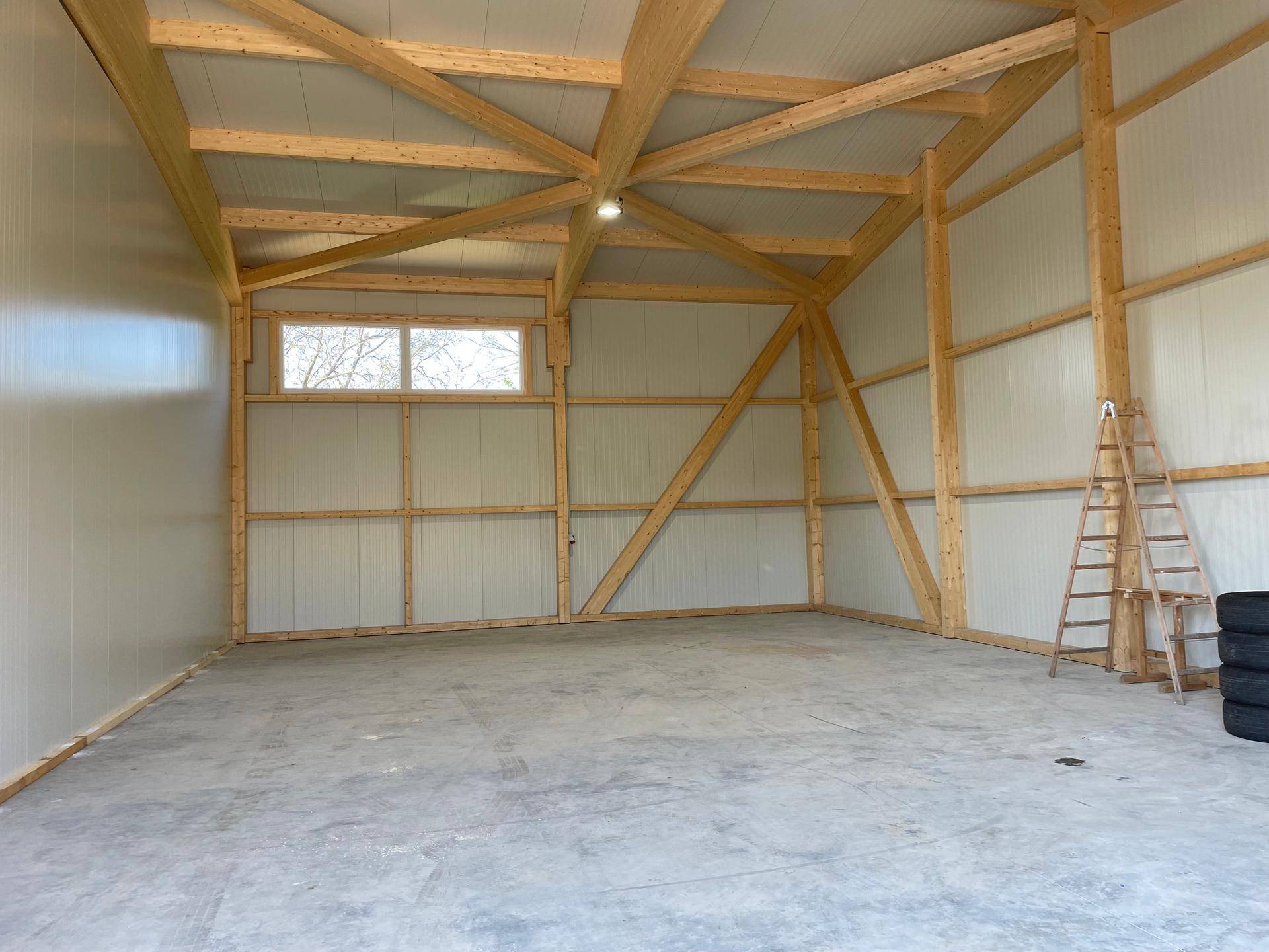Innenansicht einer leeren Lagerhalle mit hohen Decken, sichtbaren Holzträgern und einem kleinen Fenster.