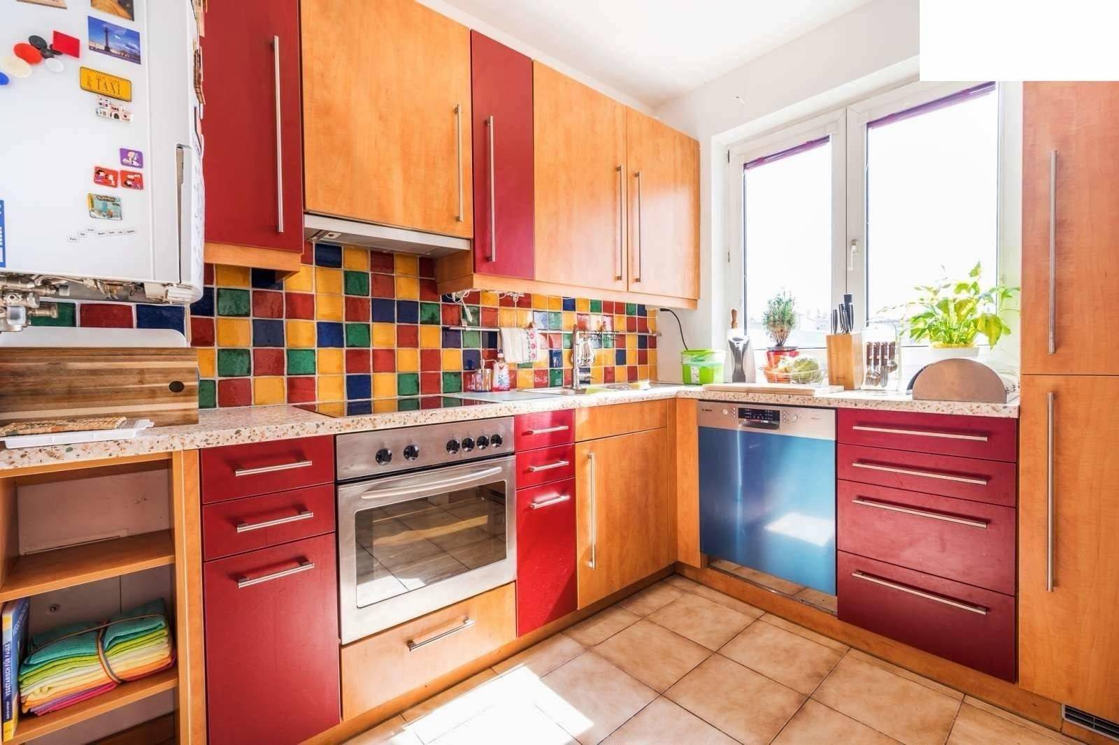 Bunte Küche mit roten und holzfarbenen Schränken, Fliesenboden und Fenster.