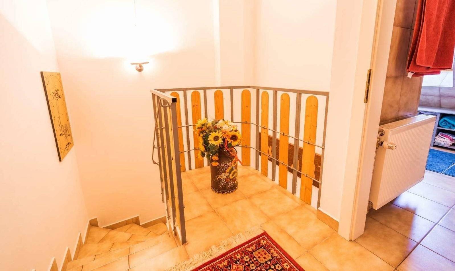 Treppenaufgang mit Fliesenboden und Geländer, geschmückt mit einem Blumenarrangement.
