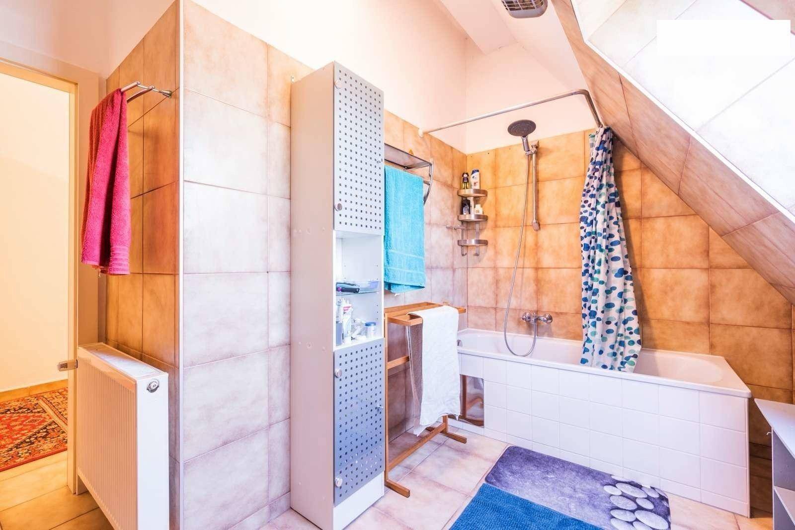 Badezimmer mit Badewanne, Duschvorhang und beigefarbenen Fliesen unter einer Dachschräge.