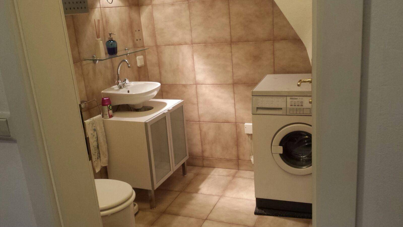 Badezimmer mit Waschmaschine, Waschbecken und Toilette, gefliest in warmen Brauntönen.